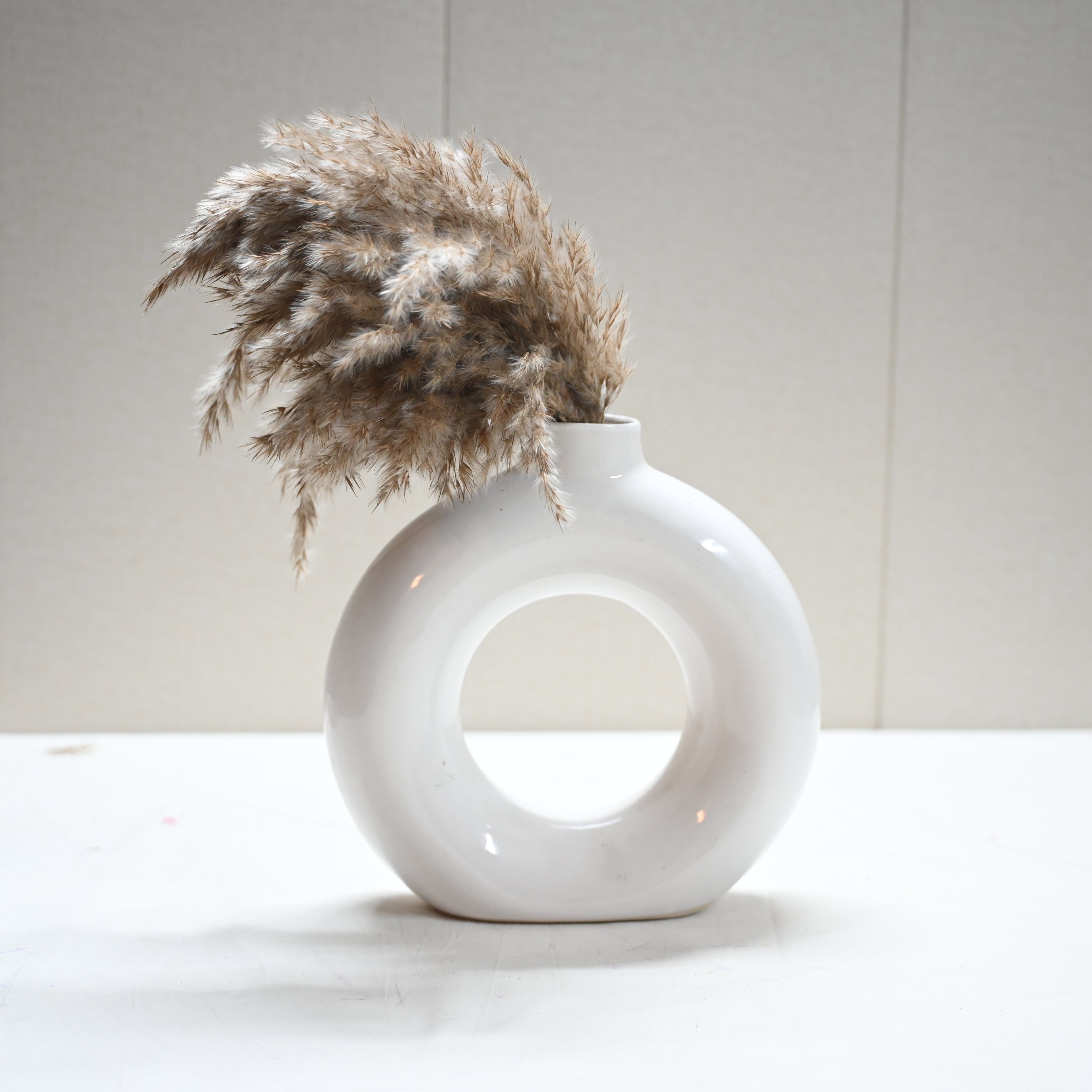 White donut-shaped ceramic vase with pampas grass